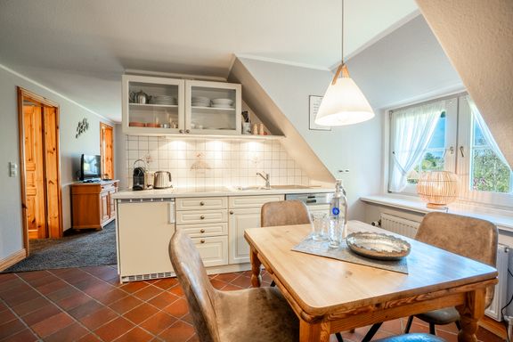 In der Küche steht ein Tisch mit 4 Stühlen unter einer Lampe in Fensternähe