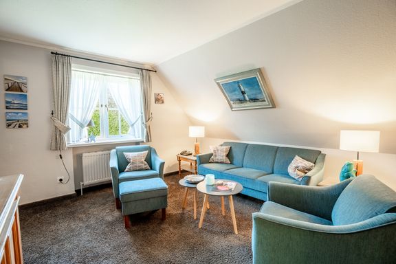 Im Wohnzimmer steht ein Sofa mit zwei Sessel und zwei kleinen Sofatischen in Fensternähe.